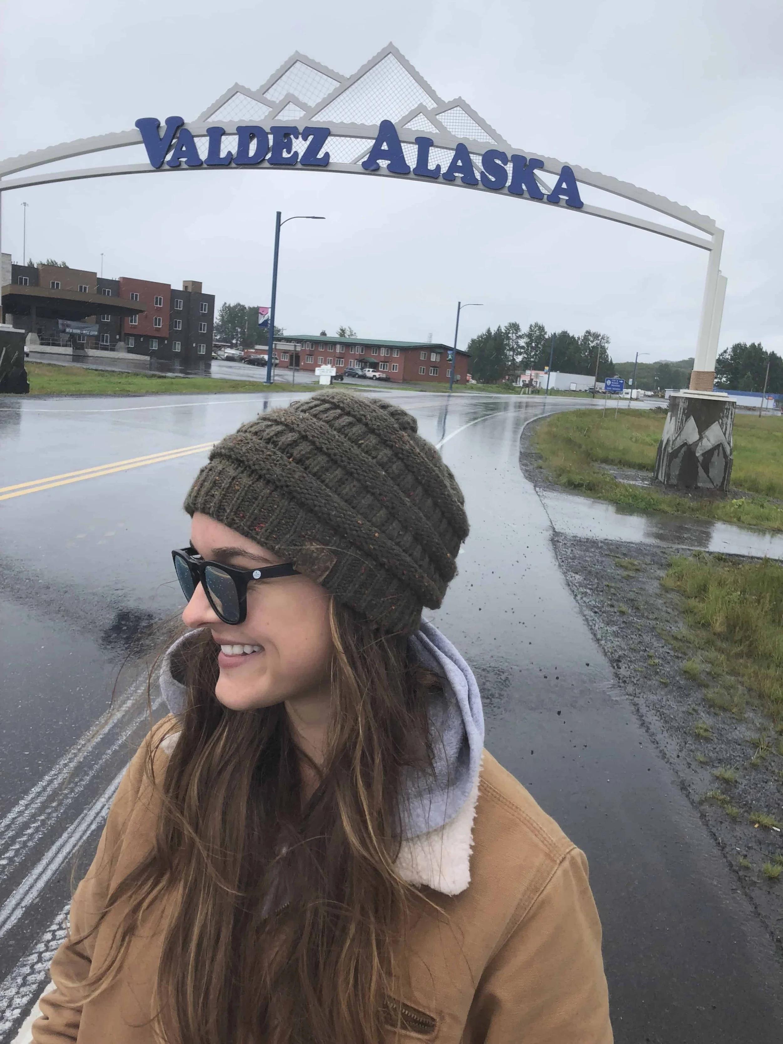 Woman smiling and looking to the side while standing beneath a Valdez, Alaska sign.