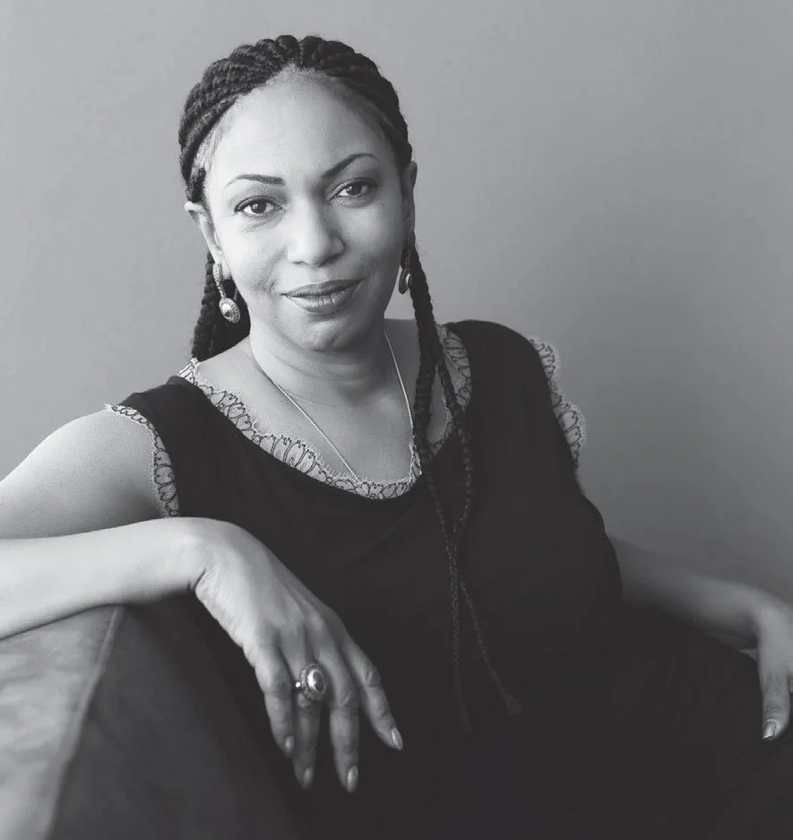 Woman with slight smile poses in chair for black & white portrait.