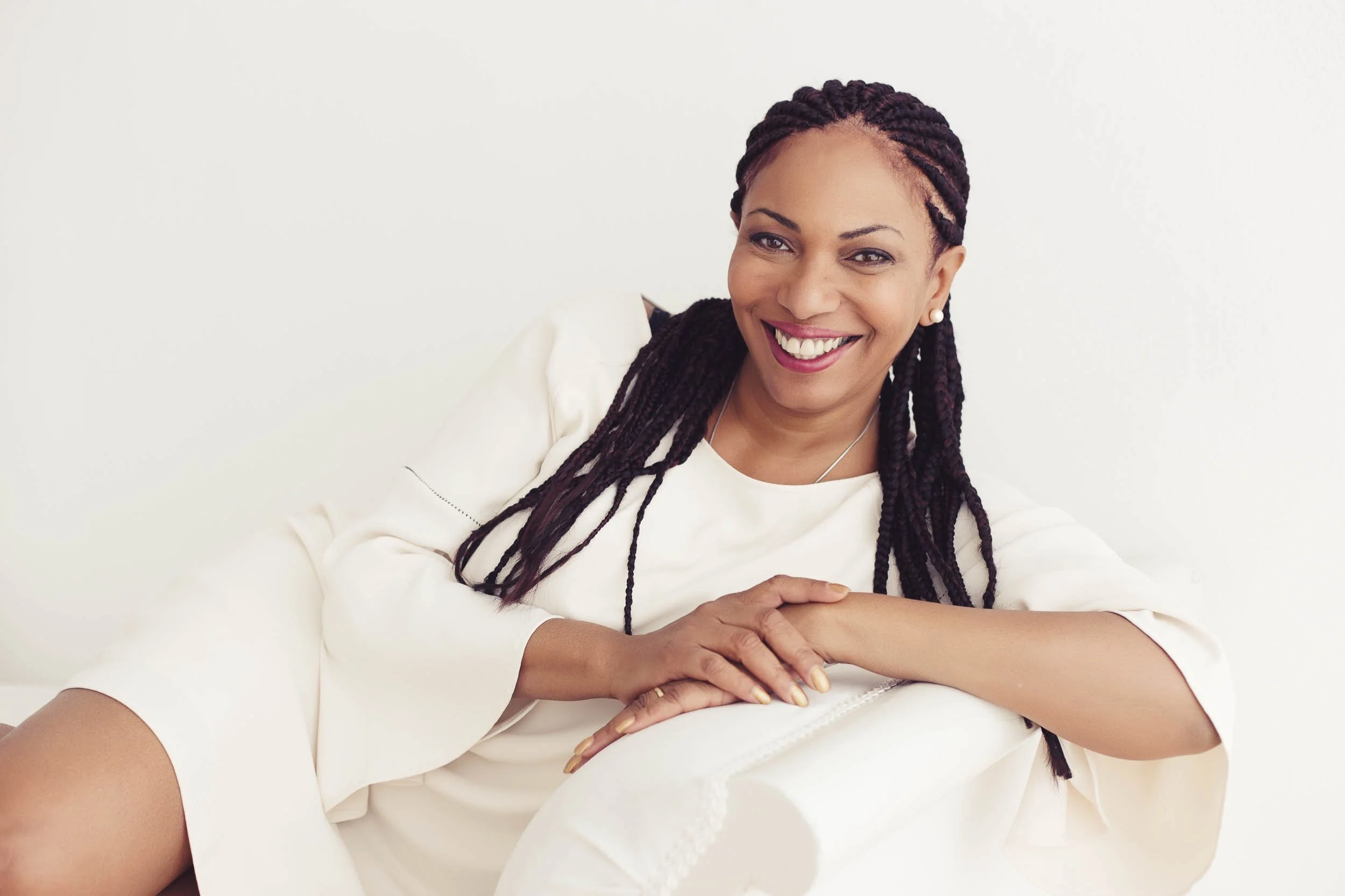 Woman dressed in all white leans on the arm of a white chair.