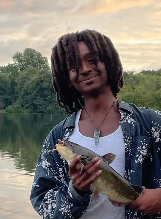 Lawrence C. Harris smiling and holding a fish by a lake at sunset, outdoors in a peaceful natural setting