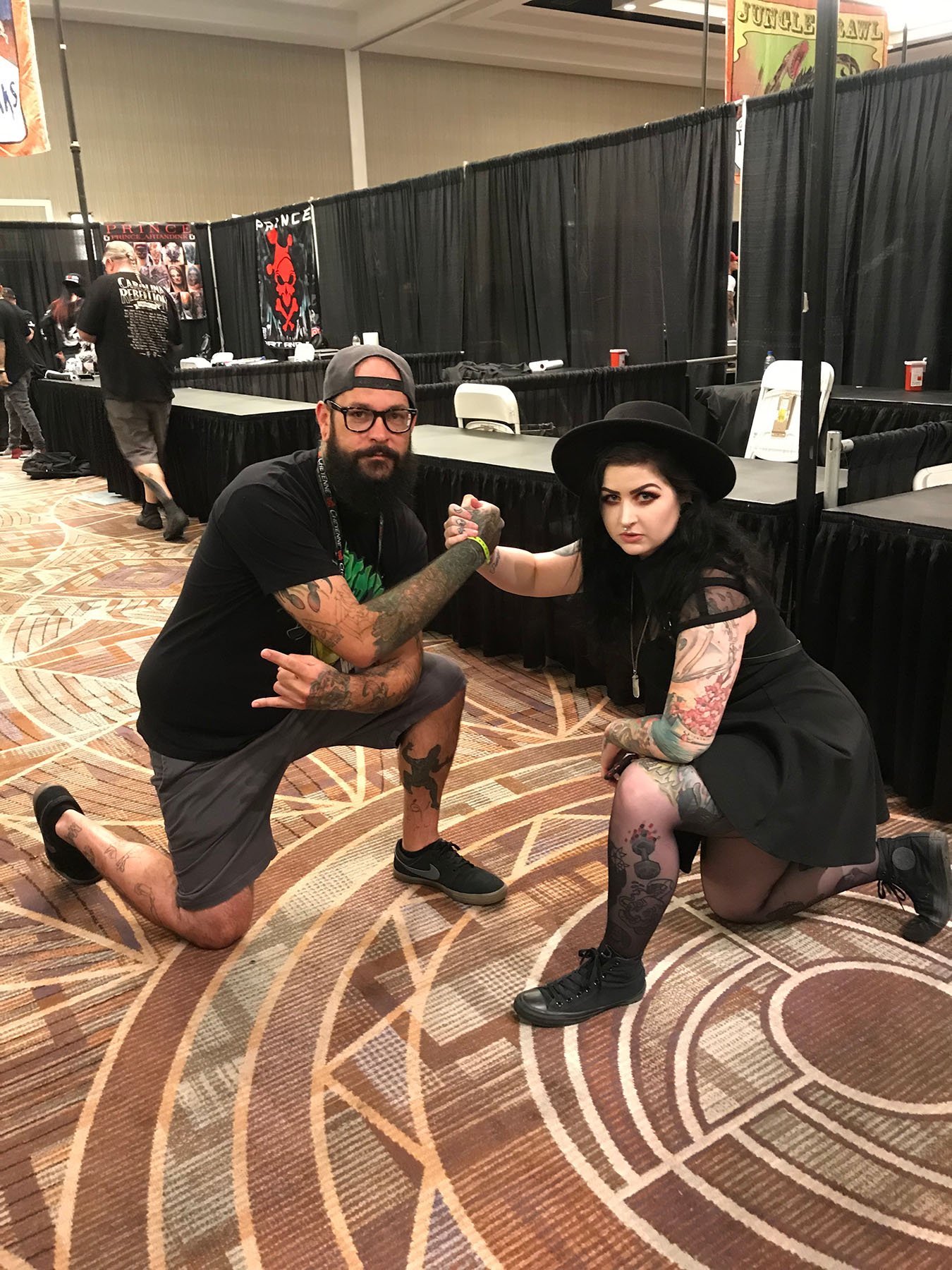 Two tattoo artists posing together at a tattoo convention booth.