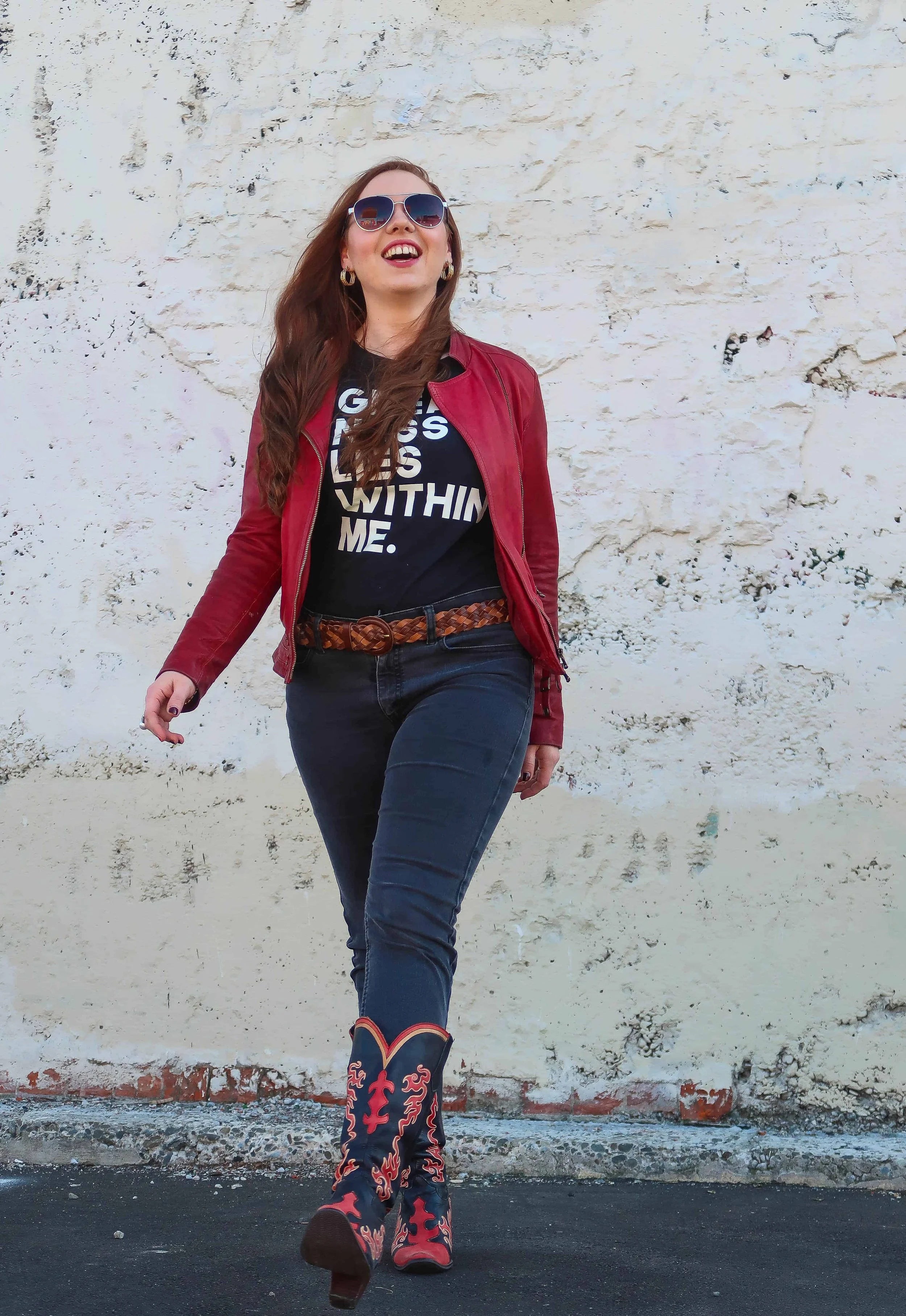 Woman posing against a concrete wall while wearing black cowboy boots outdoors.