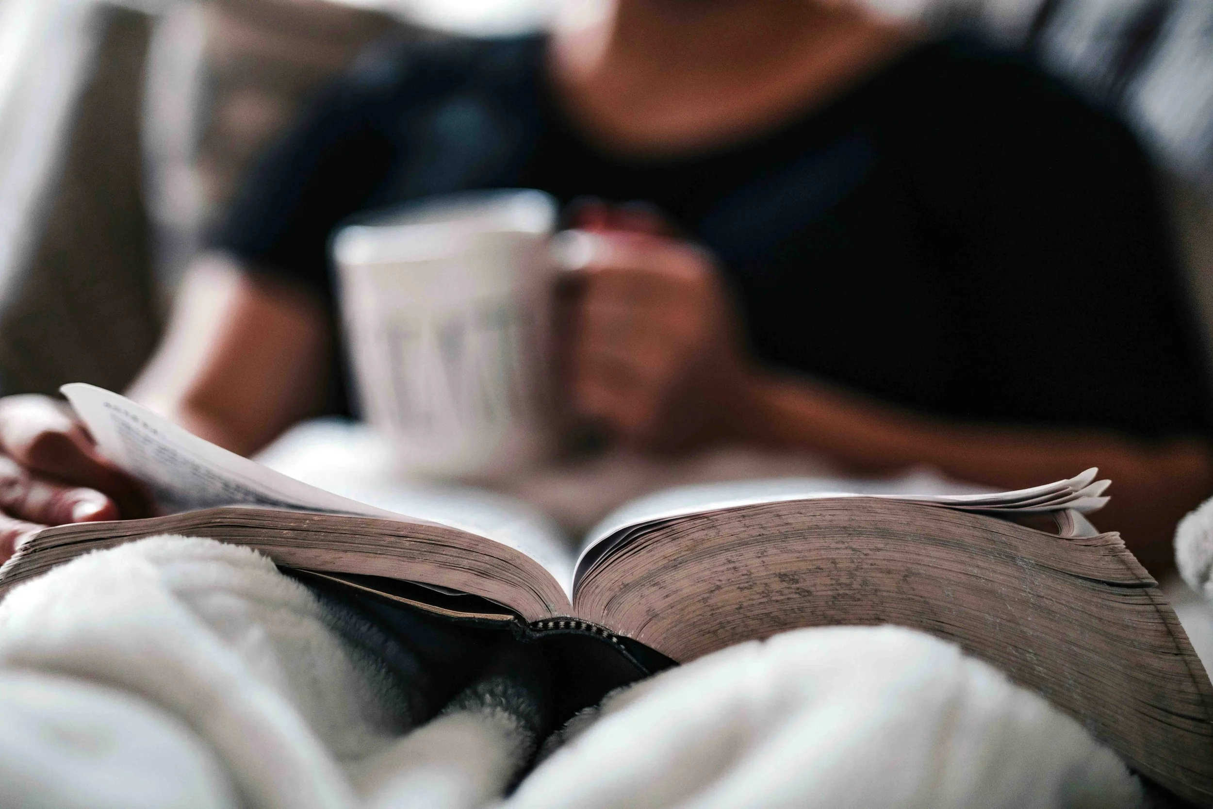 An open book and a mug of coffee on a cozy blanket, capturing a quiet moment of reading and relaxation.