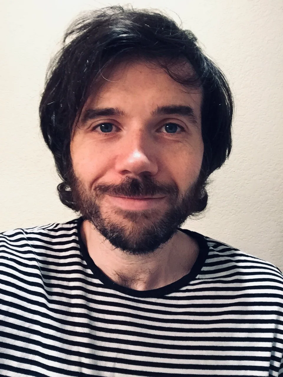 Person smiling at the camera while wearing a striped shirt against a neutral background.