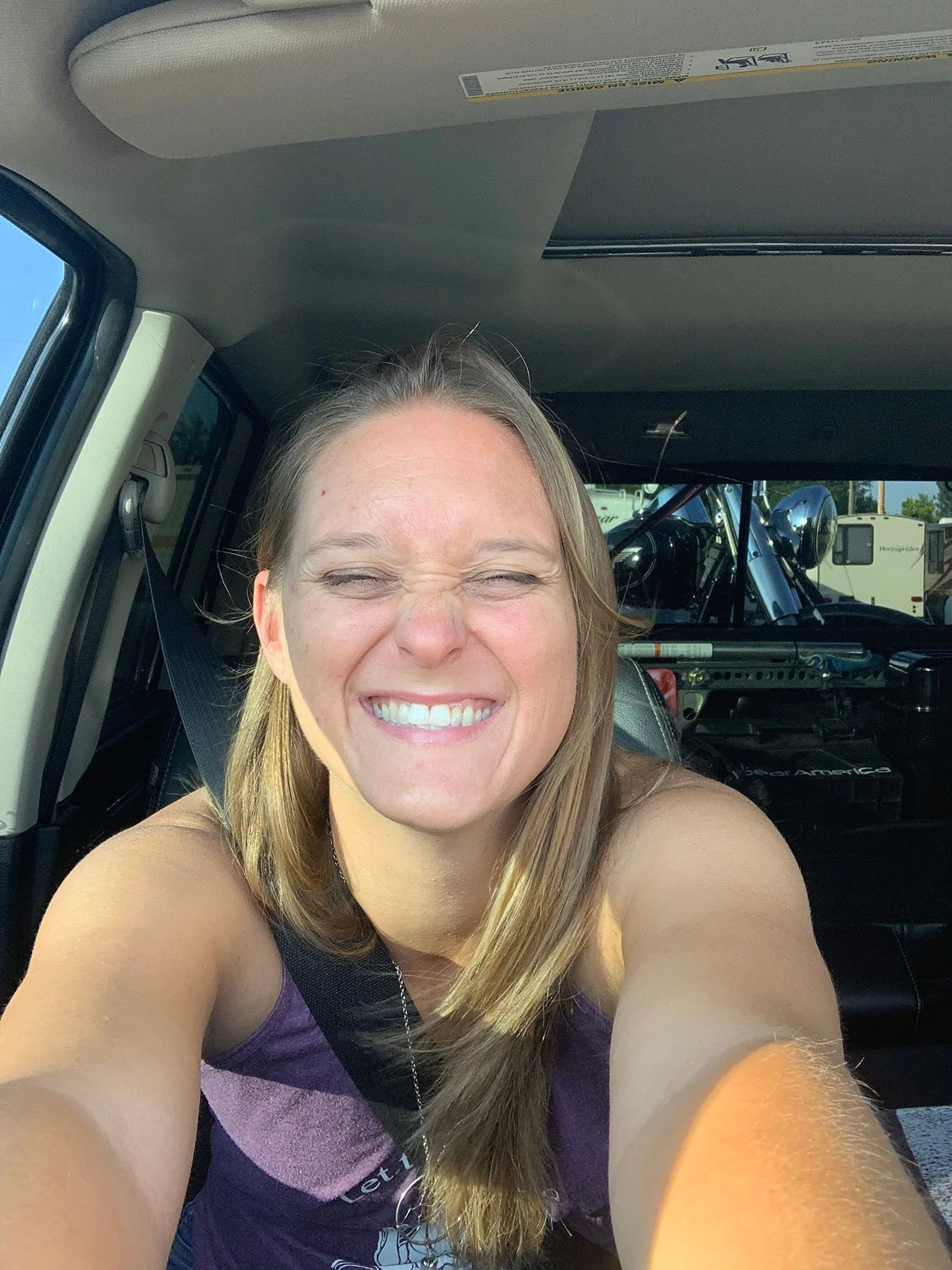 Woman smiling brightly while taking a selfie inside a car.
