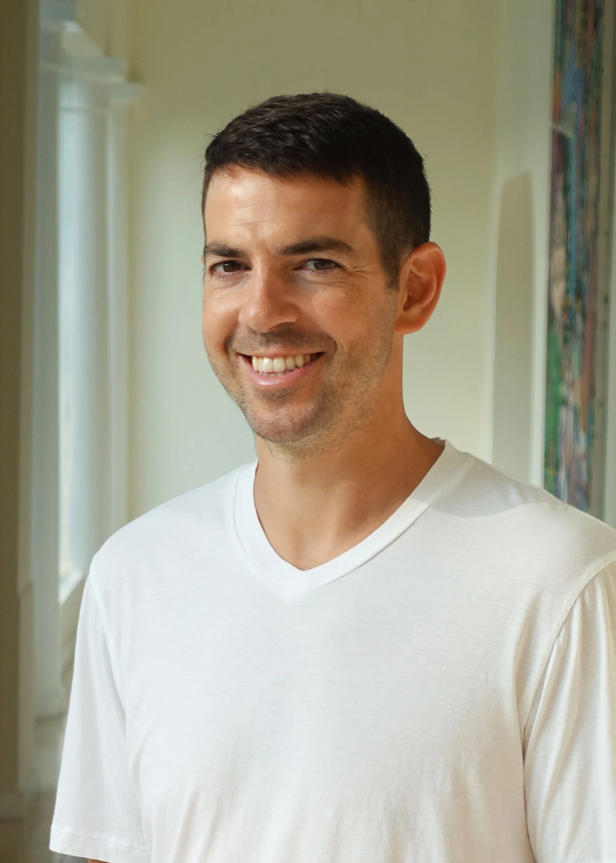 Man in white t-shirt smiles for portrait.