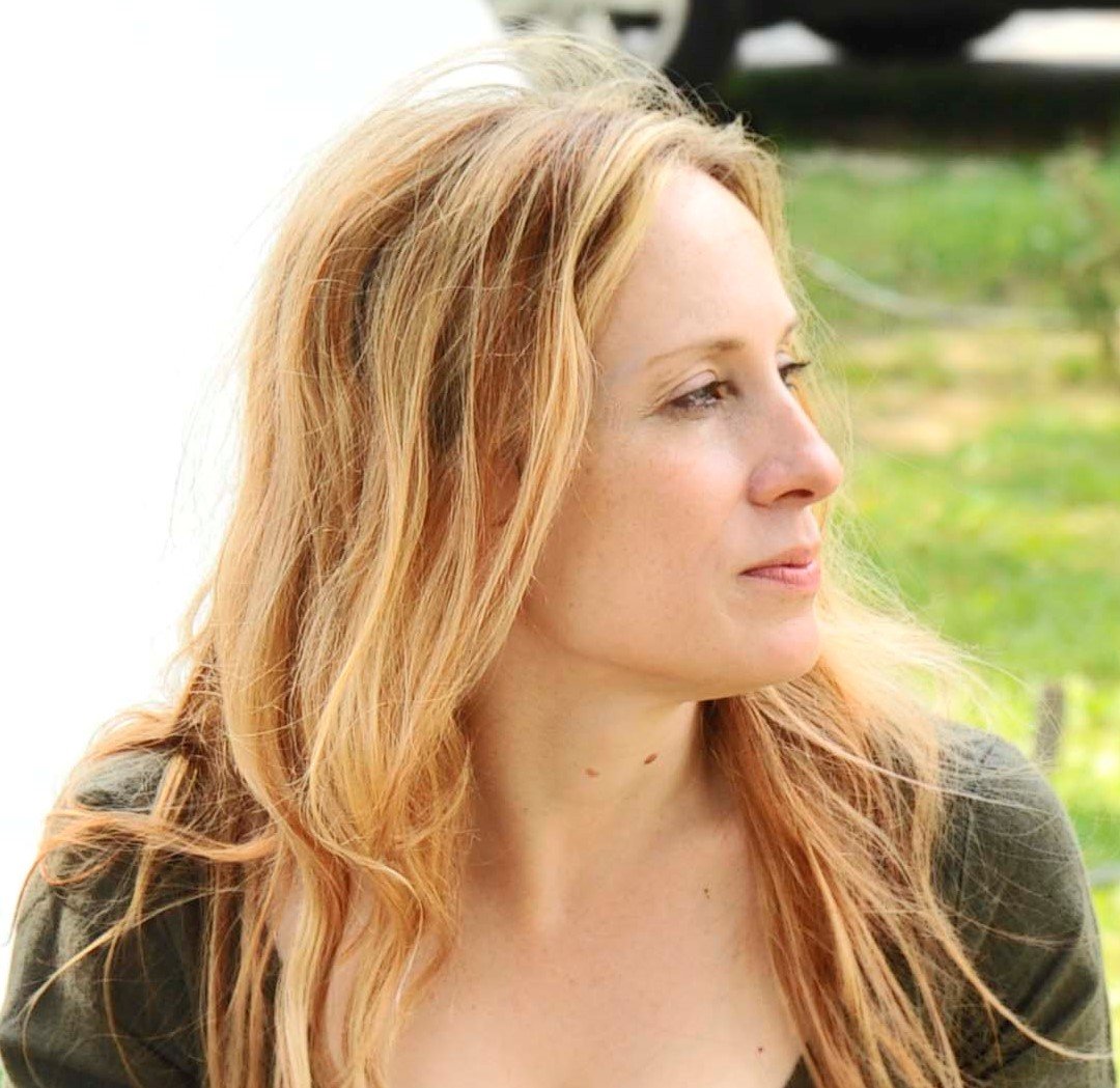 Woman with long blonde hair looking to the side outdoors.