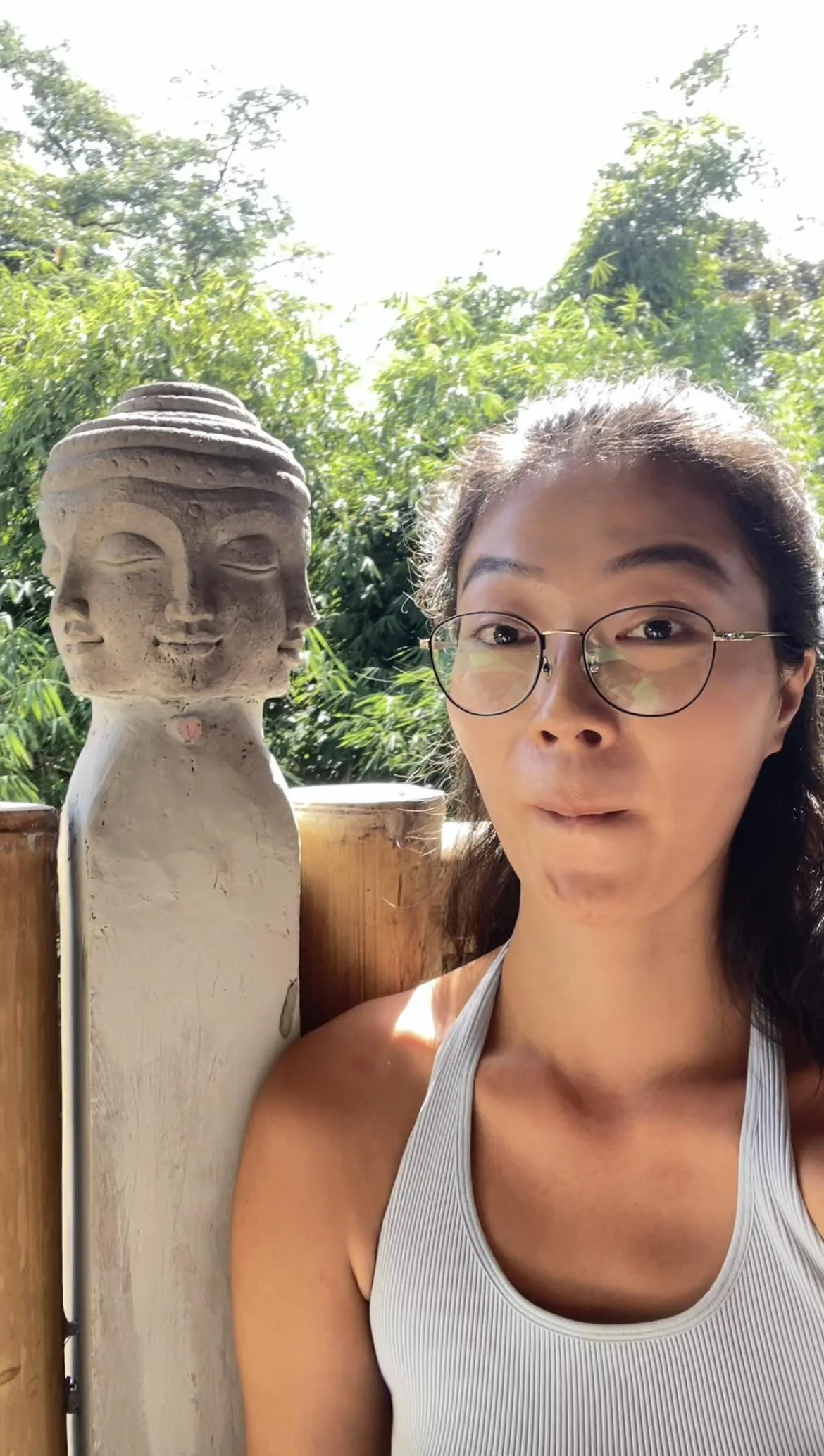 Asian woman wearing glasses and making a silly face sitting in front of a statue