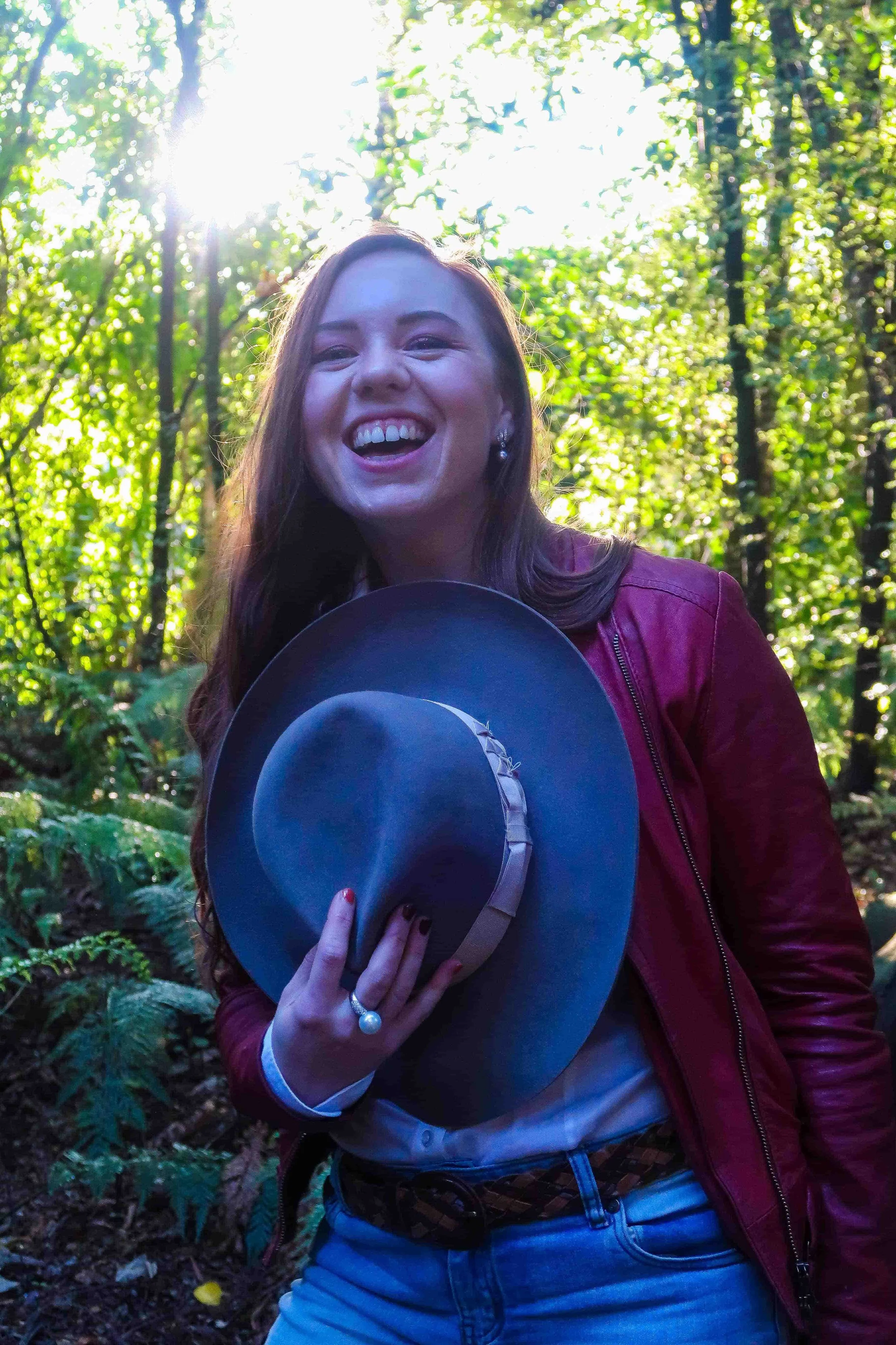 Happy woman standing in the woods while holding a cowboy hat against her chest.