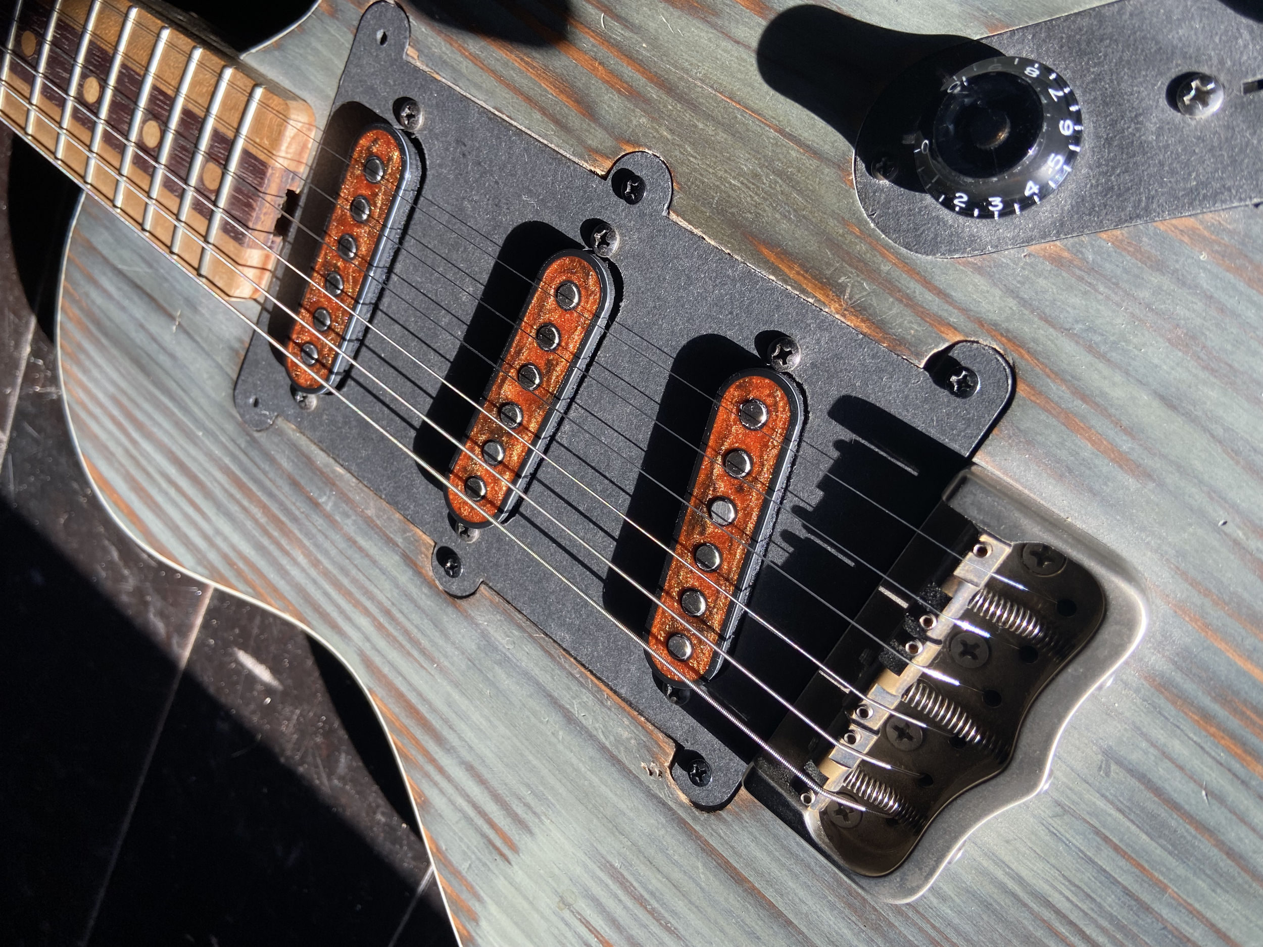 Close-up view of an electric guitar's pickups, strings, and control knob, with visible wood grain of the guitar body.
