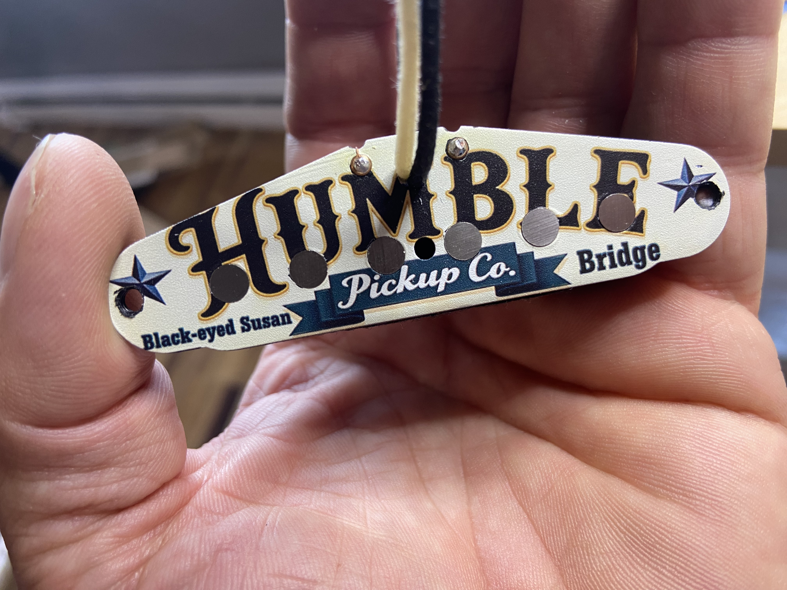 Close-up of a person's hand holding a guitar pickup with the text 'HUMBLE' and a logo on it.