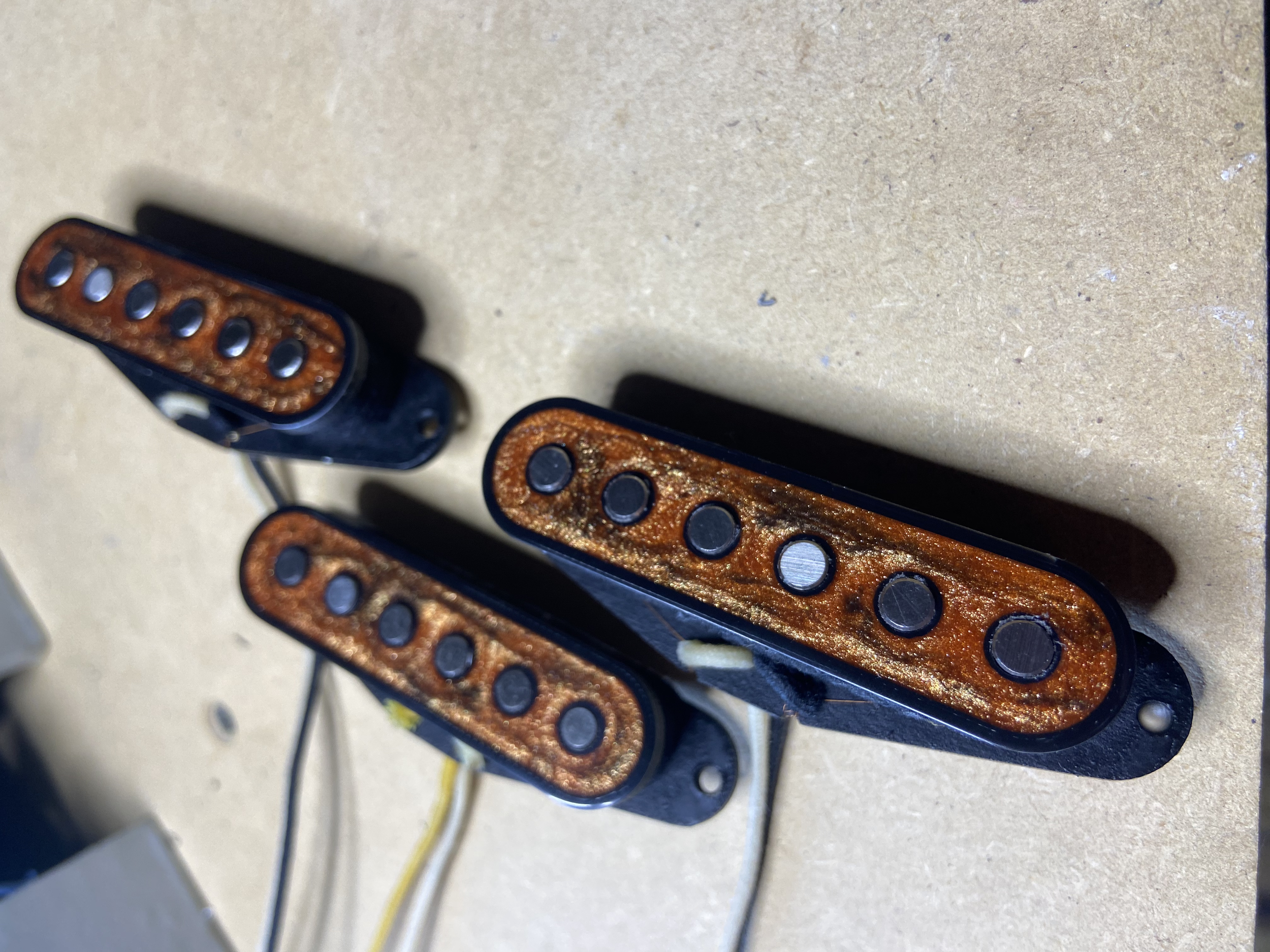Close-up of multiple guitar pickups arranged on a beige surface, showing the magnetic poles and metallic parts.