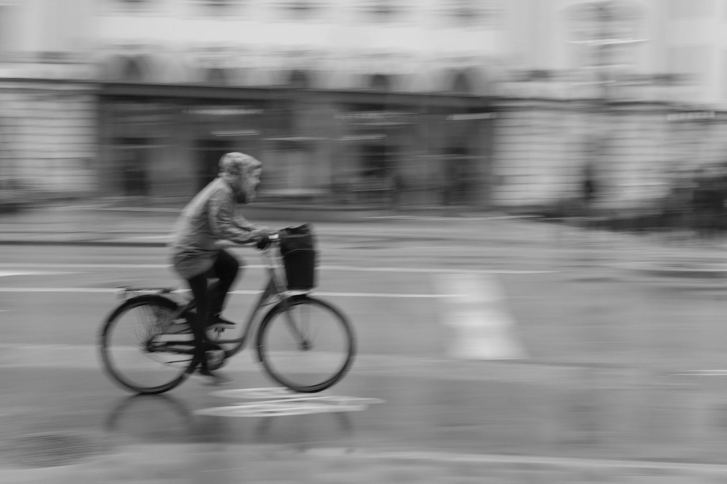 A person riding a bicycle on a street, blurred to show motion in black and white.