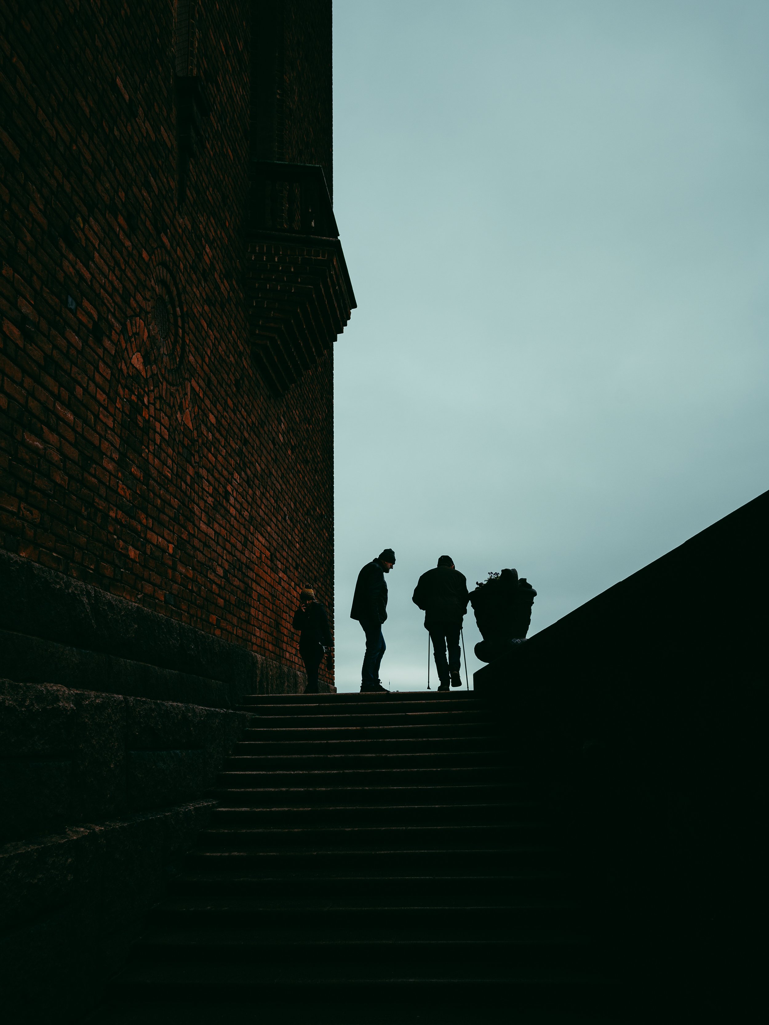 Silhouettes of three people walking up stairs outside a brick building on a cloudy day.