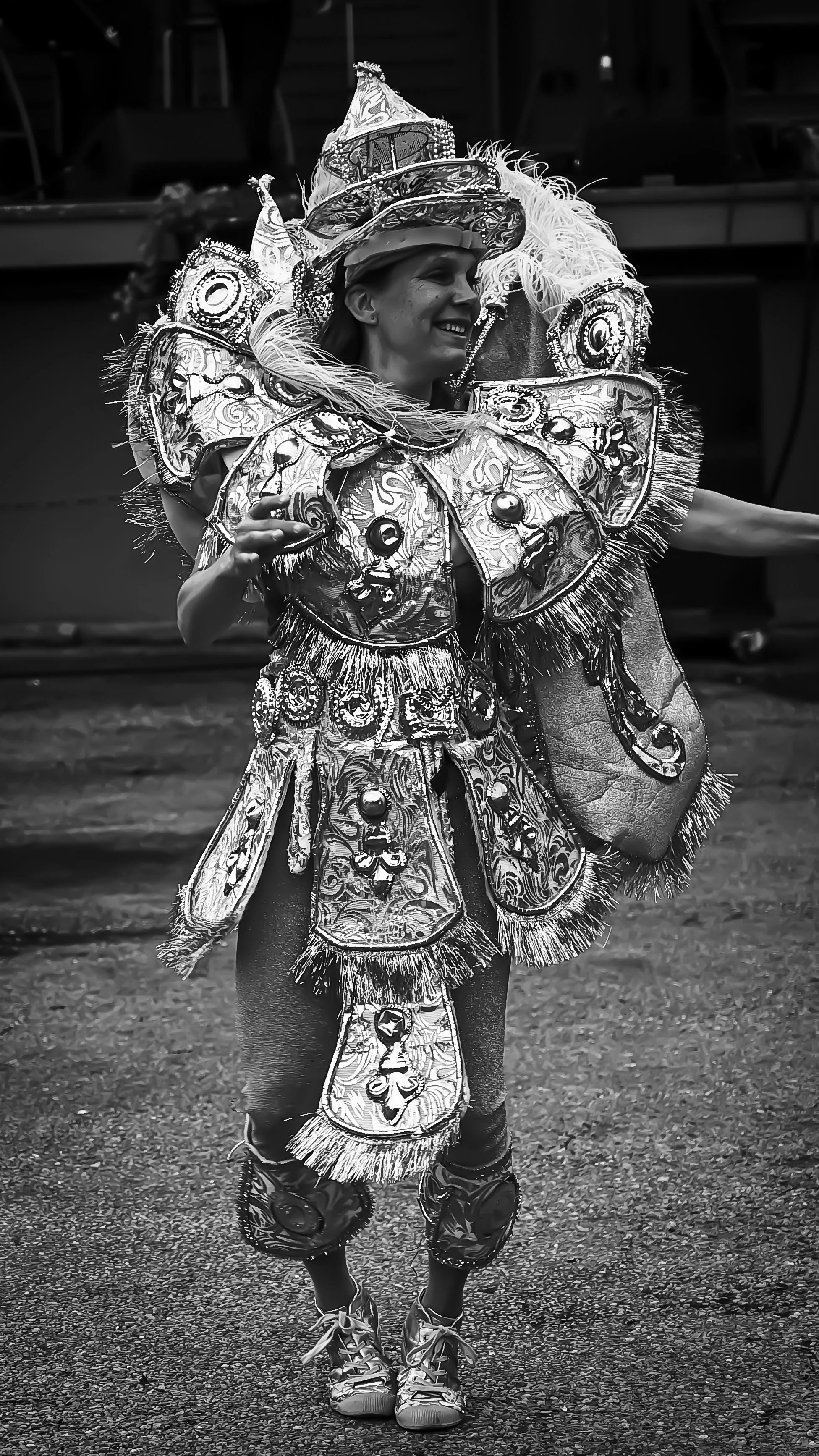 Person dressed in an elaborate, ornate costume with decorative patterns, feathers, and embellishments, possibly participating in a festival or parade, smiling and dancing.