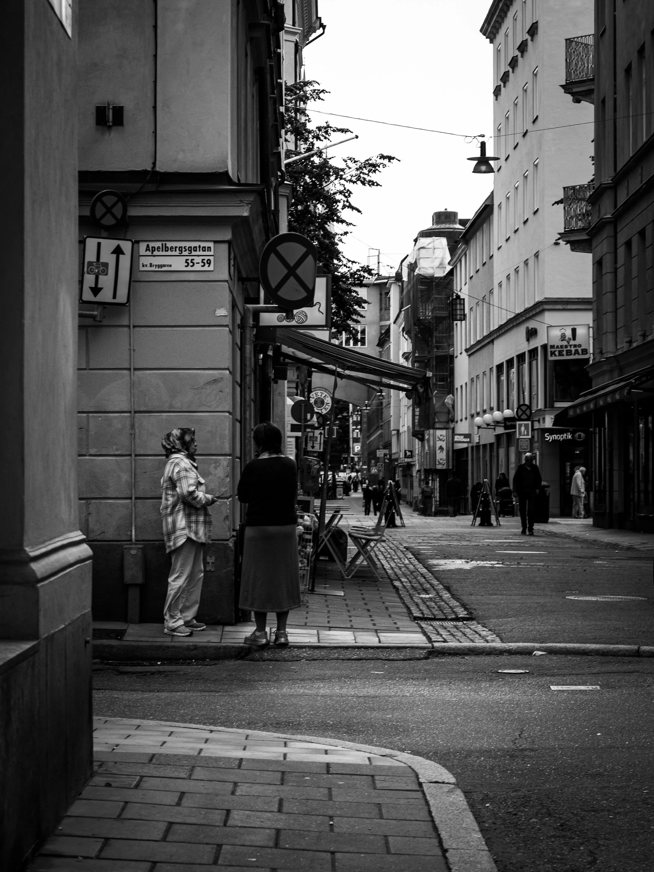 Black and white photo of an urban street scene with pedestrians, signs, and buildings.