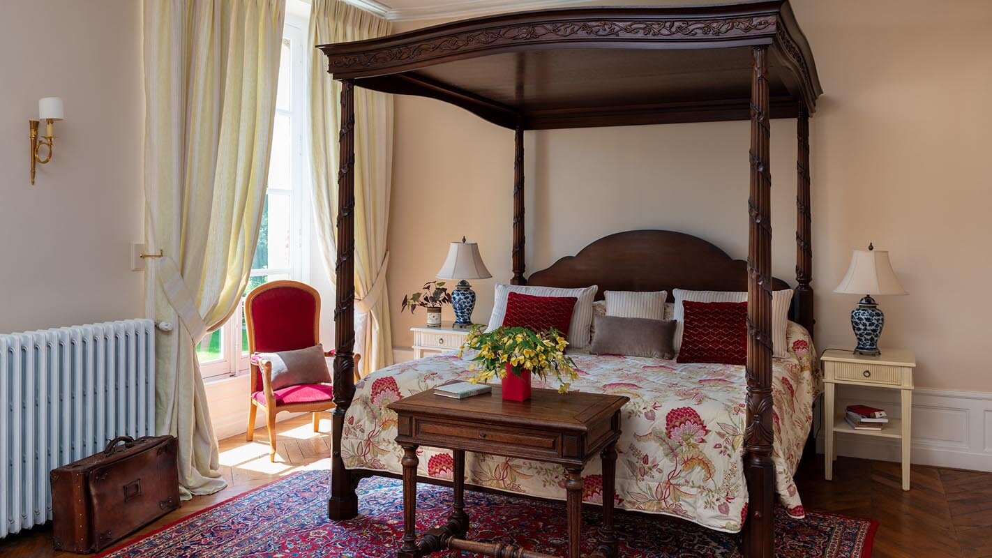 An elegant room with a four poster bed decorated with white and red bedding available for rent at the chateau.