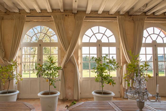 A room with large french windows decorated with potted plants, available to rent in a chateau near Paris for a special event.