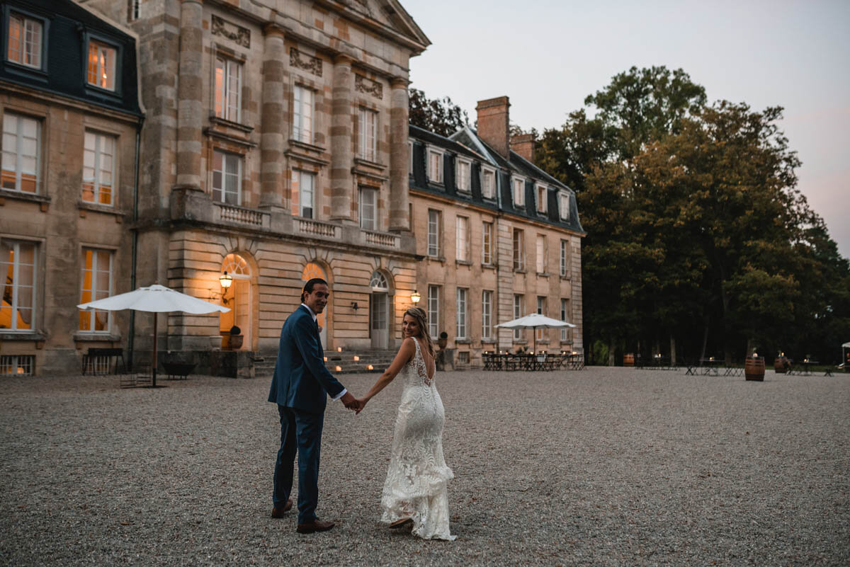 A bride and groom holding hands in front of Chateau de Courtomer, a French chateau wedding venue.