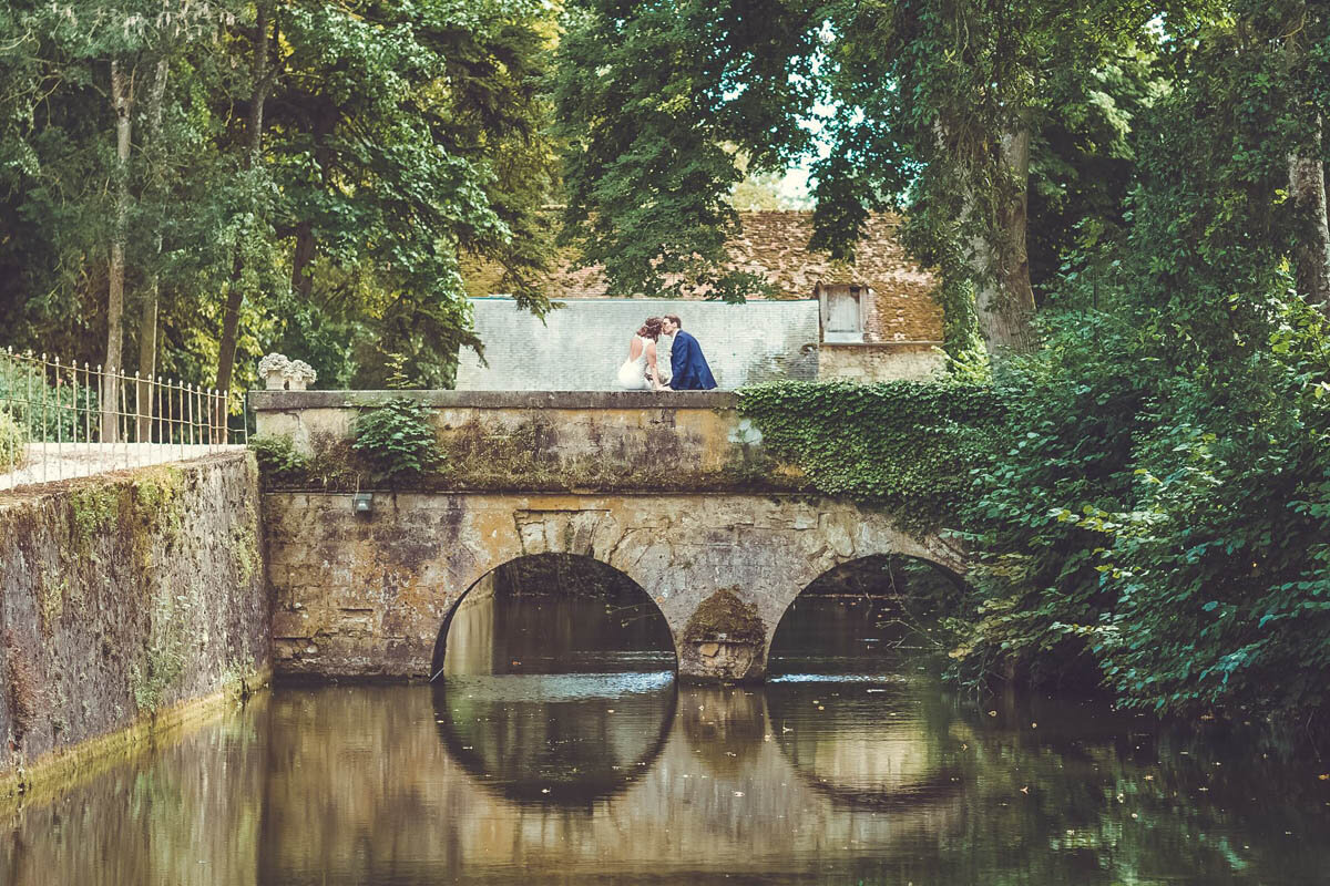 A bride and groom standing on a bridge over a moat near a French chateau wedding venue.
