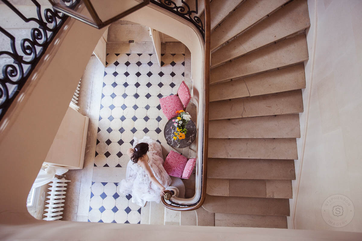 An aerial view of a bride at the bottom of a stairwell in a white dress at a French chateau wedding venue.