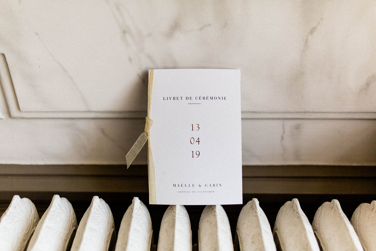 A wedding program resting on a radiator and leaning on a marble wall at the chateau.