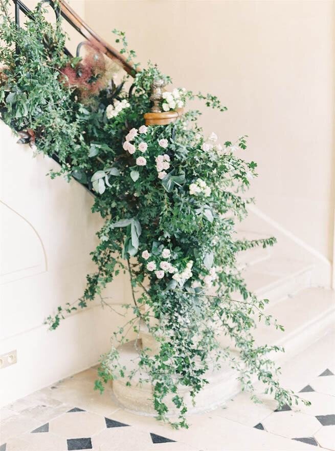 A stone staircase adorned with lush greenery and blooming flowers, reminiscent of a French chateau wedding venue.