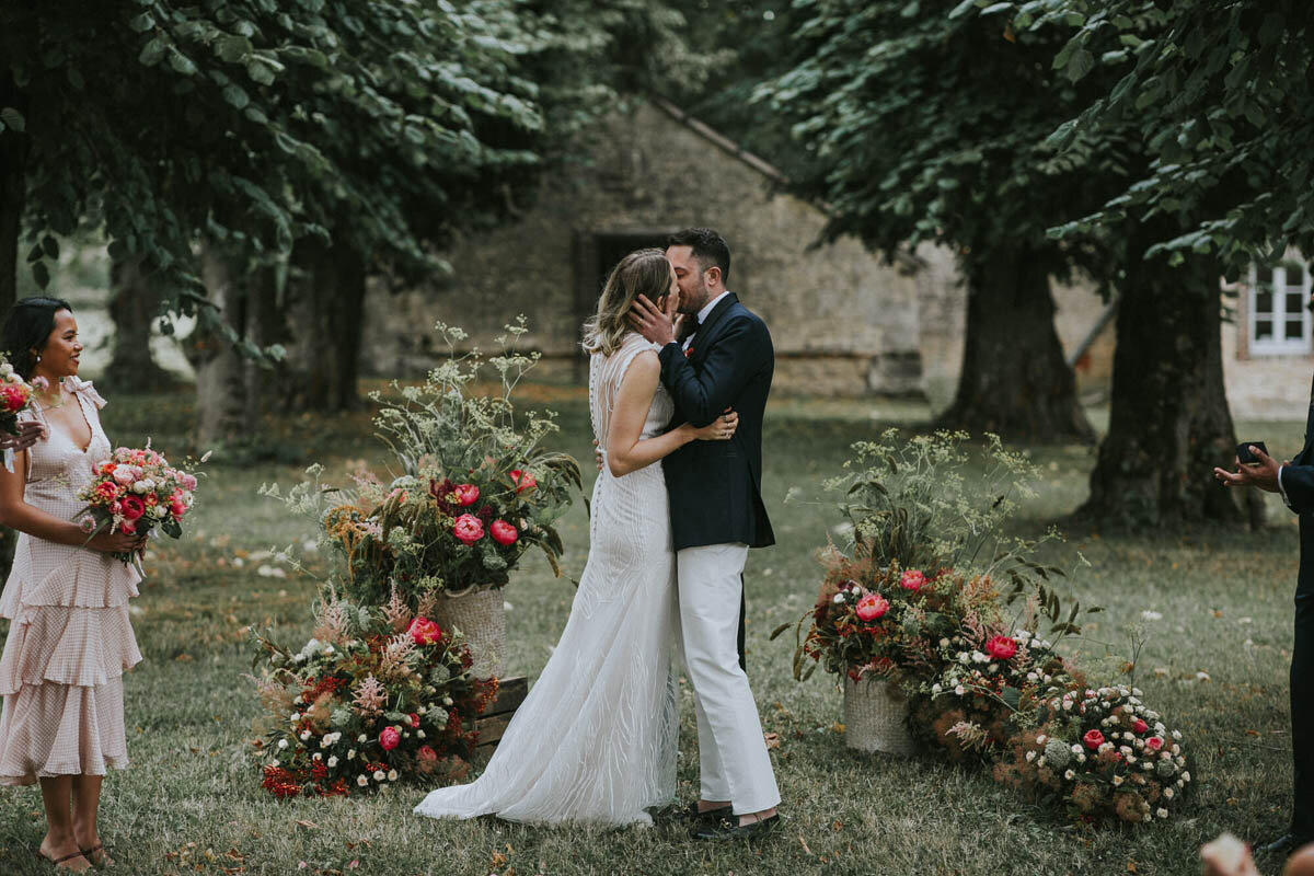 A bride and groom kiss in front of a large group at a beautiful chateau wedding venue in France.