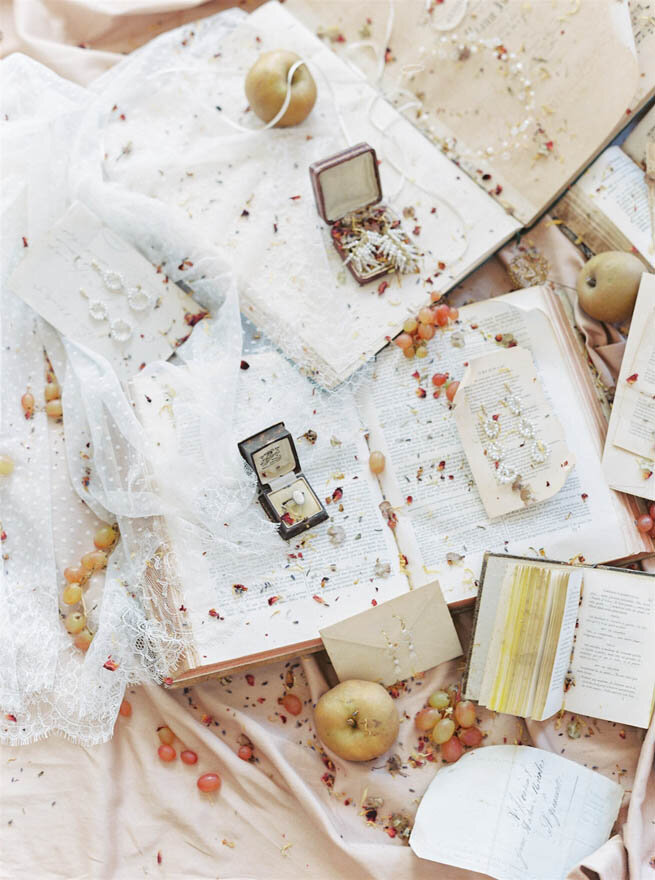 Wedding ring boxes and jewelery lying on top of books with fruit scattered artistically.