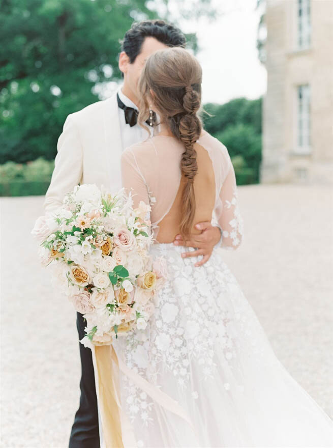 A bride and groom kissing in front of Chateau de Courtomer, a French chateau with extensive grounds.