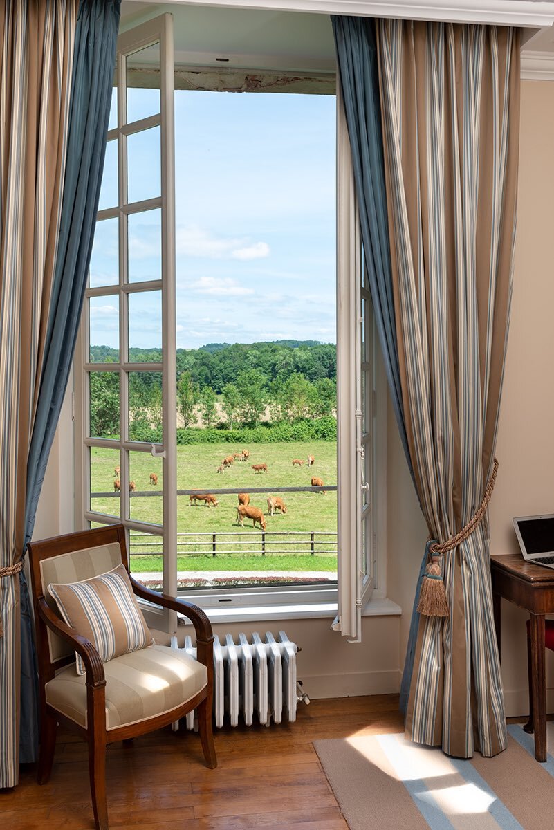 A contemporary room with a large window overlooking the farm where cows are grazing, available for stays at a french chateau.