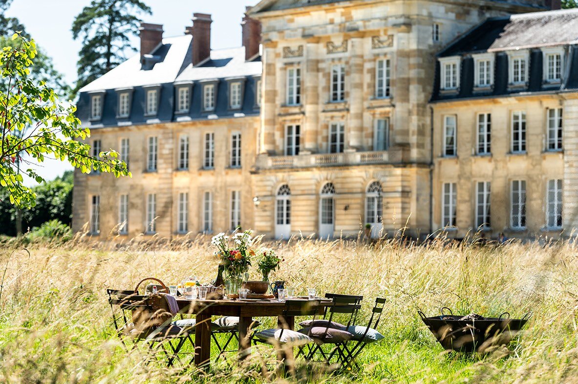 A table and chairs set in the grass in front of Chateau de Courtomer, a beautifully restored French chateau available to rent.