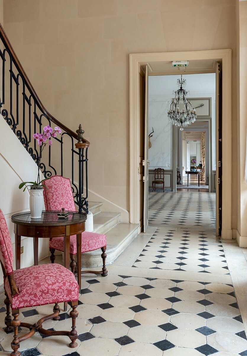 A hallway with pink chairs and a chandelier at a Chateau available to rent, near Paris.