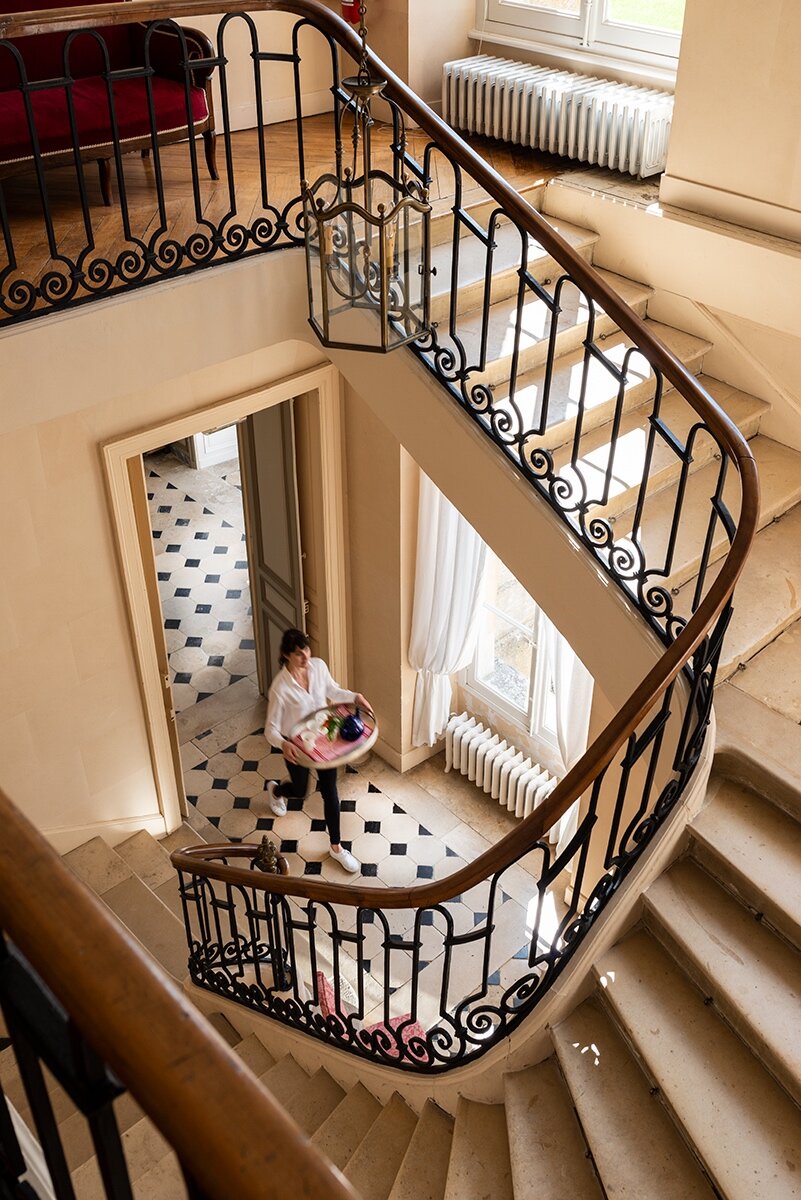 A woman carrying a tray of drinks at the bottom of a winding staircase in a Courtomer, a chateau near Paris.