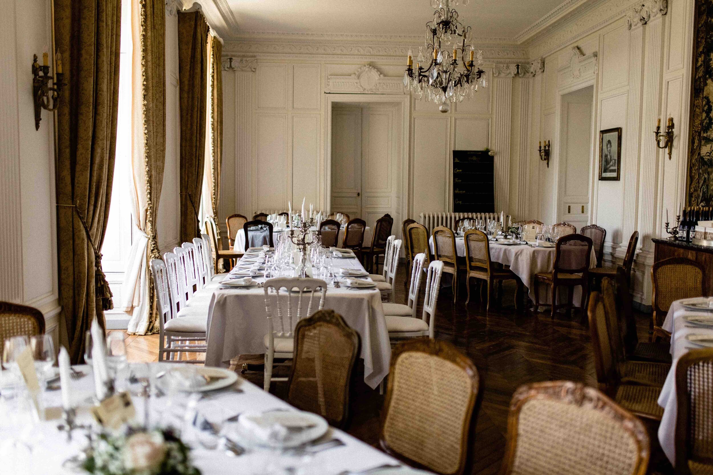 A grand dining room with long tables decorated for a wedding reception at Chateau de Courtomer.