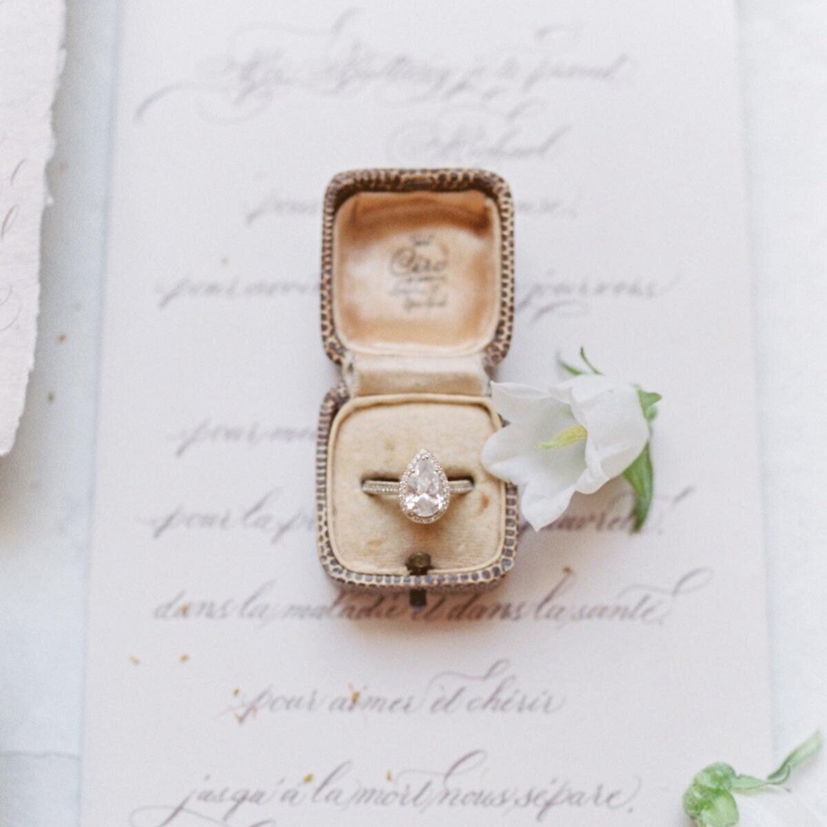 An engagement ring rests on an old book with a white flower at a wedding.
