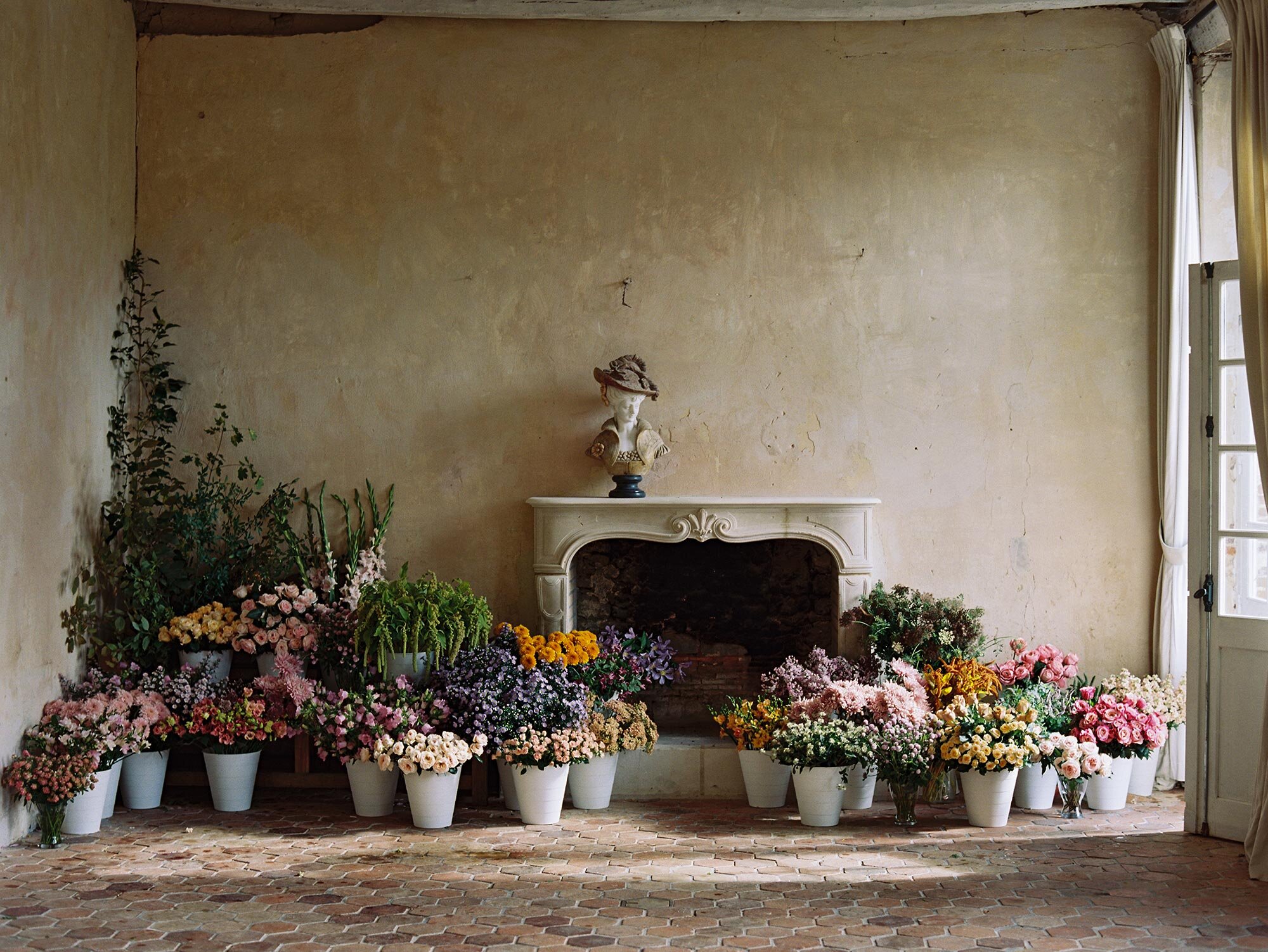 A room filled with pots of flowers and a fireplace created during the Ponderosa and Thyme workshop, a workshop at a French chateau.