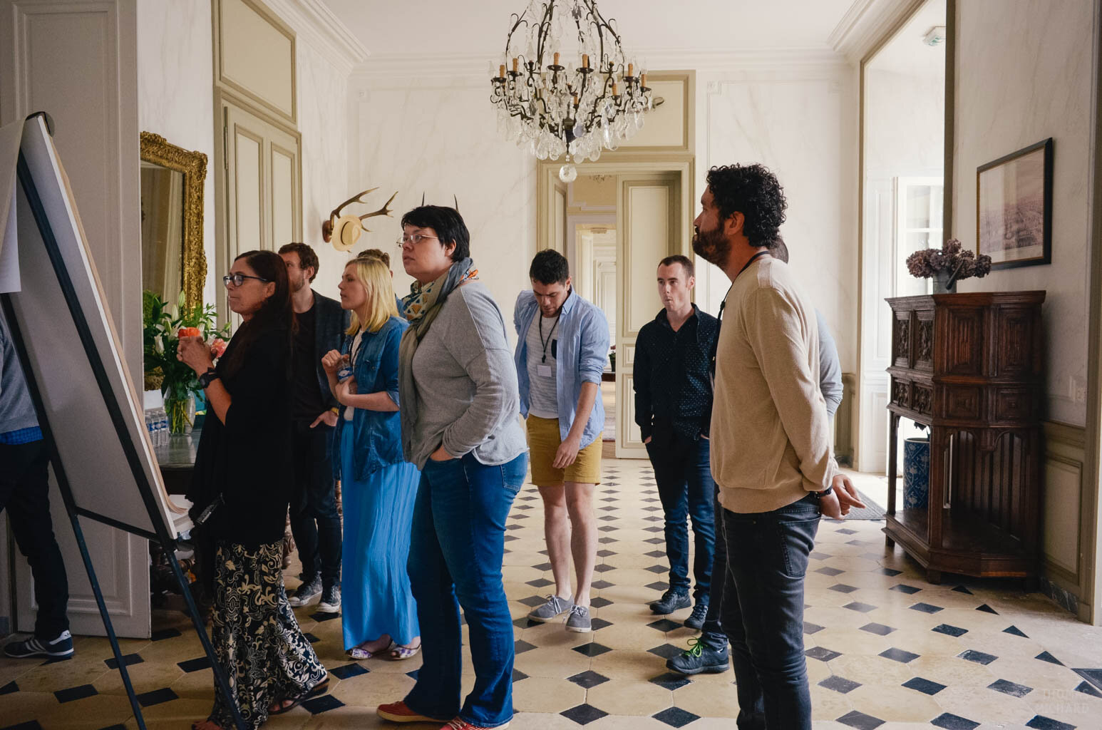 A group of people standing in room under a chandelier during a workshop or a retreat in France.
