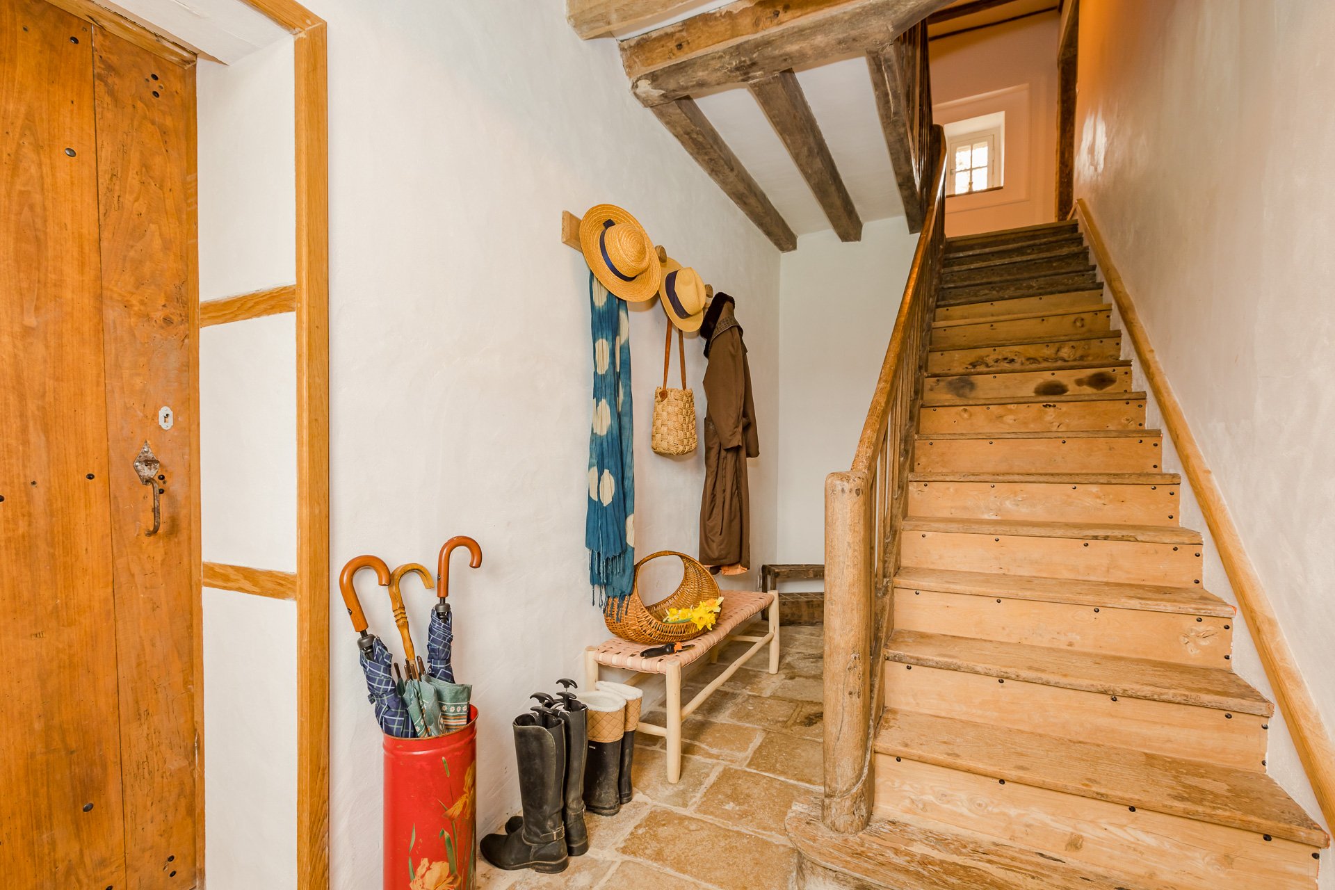 The entrance hall featuring a coat rack and and oak staircase in a French farmhouse to rent in Normandy.