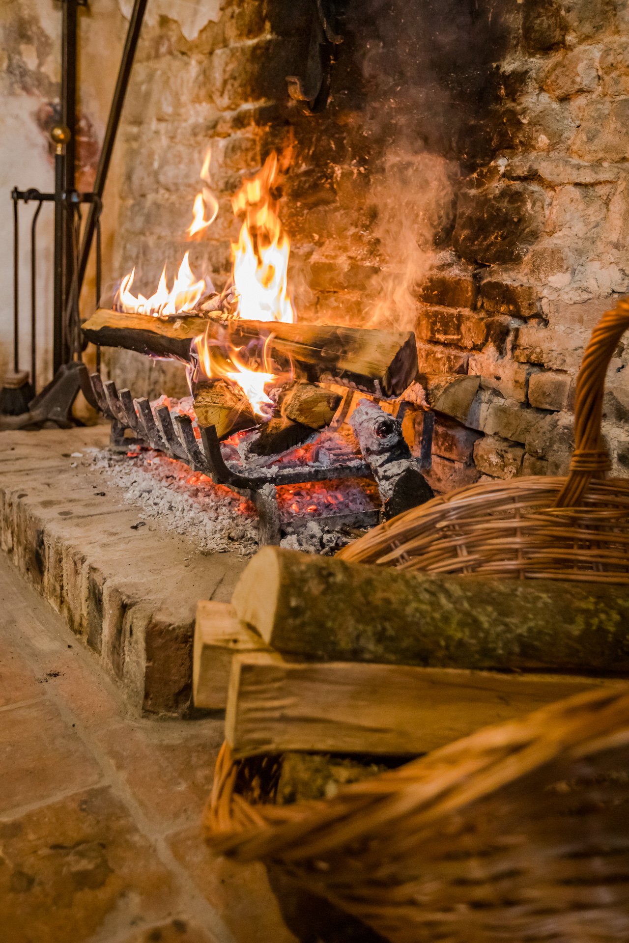 A  blazing open fire  with logs and a basket in front of it, perfect for a holiday cottage rental in Normandy.