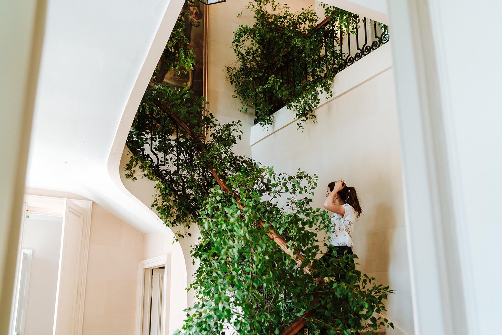 A woman on the staircase with lots of green plants decorating the railings at Chateau de Courtomer, a chateau in France.