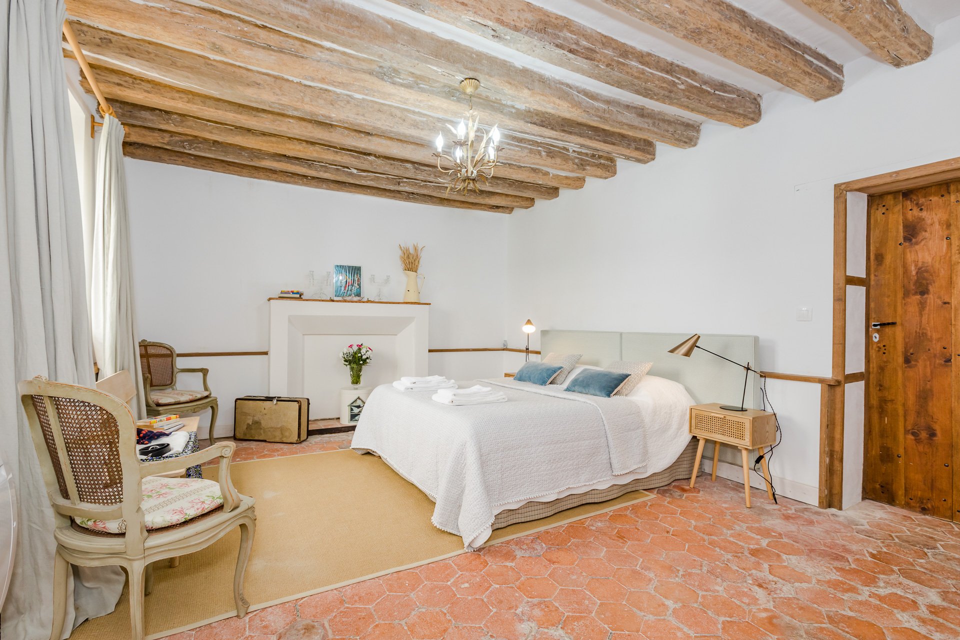 A ground floor ensuite bedroom with wooden beams and fireplace, part of a farmhouse available for rent near Paris.