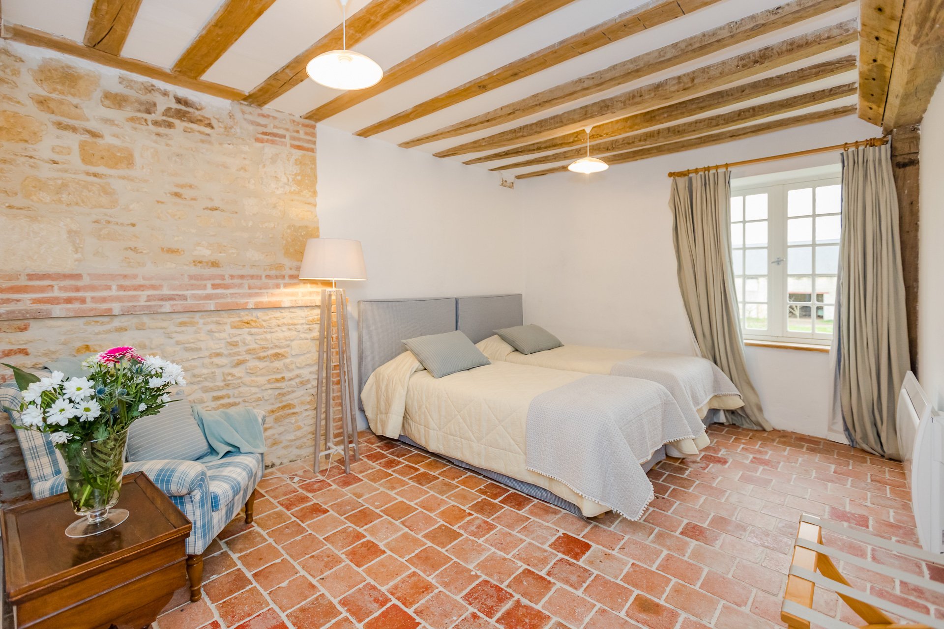 A bedroom with wooden beams and tiled floors available for rent in a French chateau near Paris.