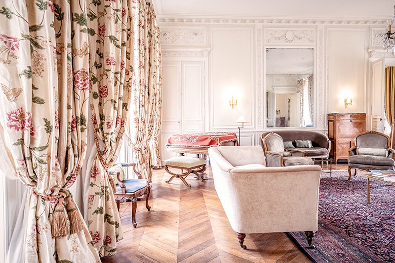 A luxurious but relaxed living room with ornate silk curtains and a grand piano at Chateau de Courtomer, near Paris.