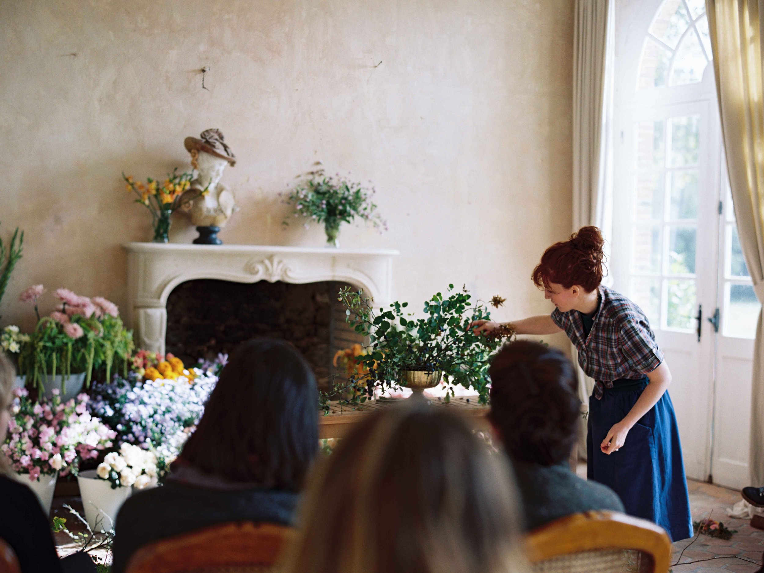 A woman is standing in a room full of flowers during a floral  workshop at Chateau de Courtomer.