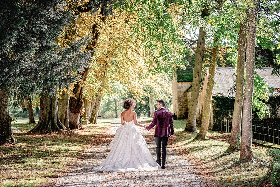 A  laughing bride and groom stroll down the path towards the Orangerie at a Chateau de Courtomer, a chateau wedding venue.