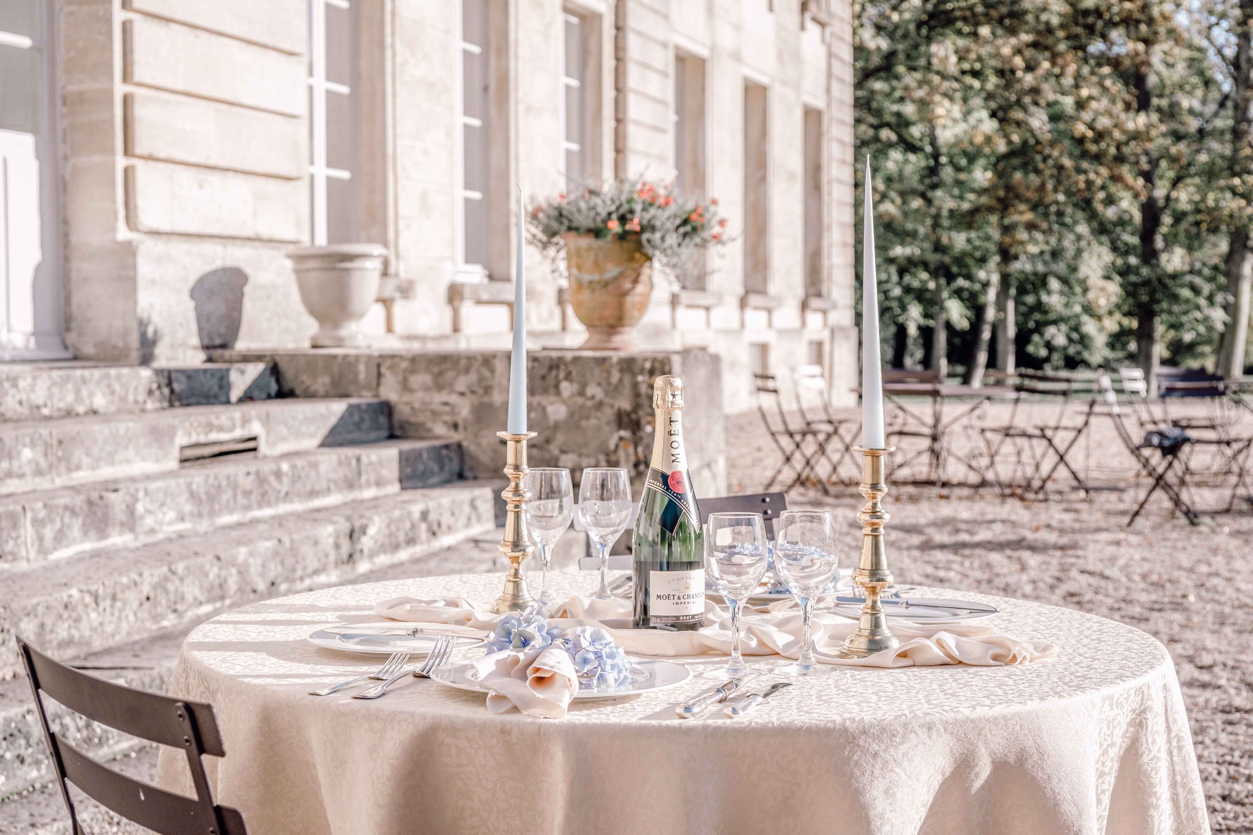 An intimate, alfresco dining table, set with candles,  decorated with pastel flowers waits for lovers  in front of Chateau de Courtomer, a French chateau wedding venue.