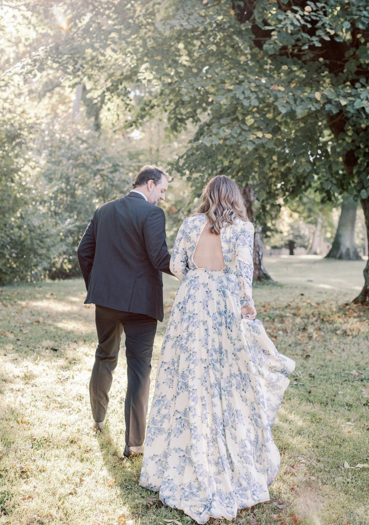 A couple holding hands strolling across the lawn with the sun beaming down on them during an event at Chateau de Courtomer.