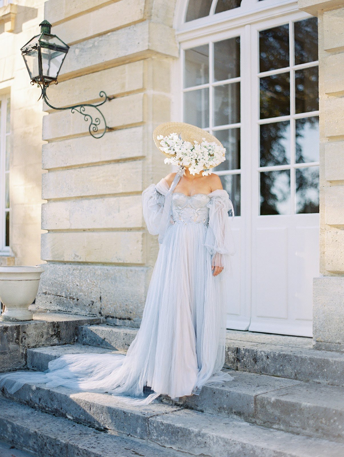 A woman in a, Bridgerton inpsired, blue wedding  dress is standing on the steps of a wedding chateau in Courtomer, France.