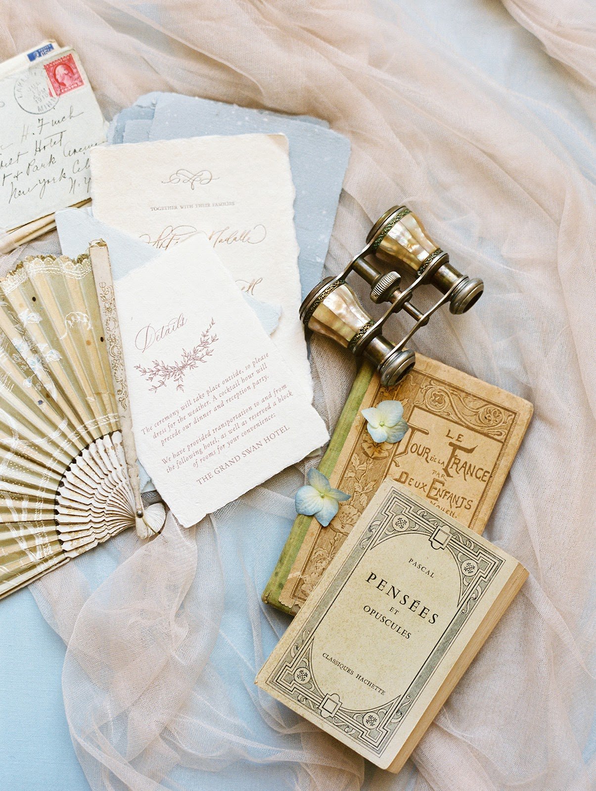 A book, fan and wedding invitation displayed on a bed in a French chateau wedding venue.